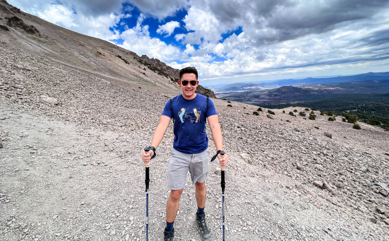 At the top of a mountain trail with hiking poles, valley behind